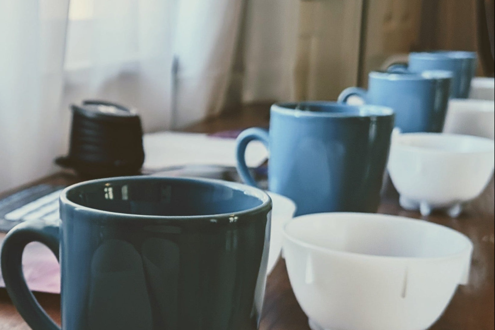 Table with various cups and bowls, including a stack of white cups and a blue mug for the cupping process.